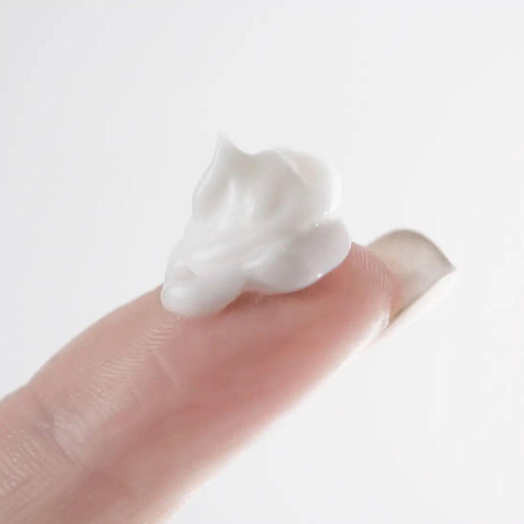 By Valenti white cream on a finger against a light gray background