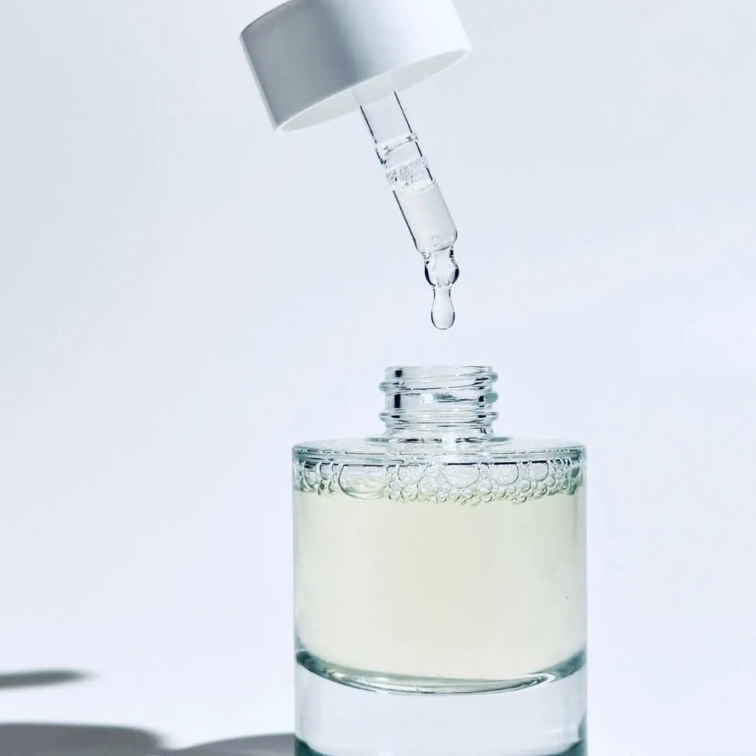 A clear glass dropper bottle of BY VALENTI Barcola Azzurro Mare Replenishing Elixir with pale aqua-green liquid inside, shown with a white dropper above it dispensing a single drop of serum against a clean white background.