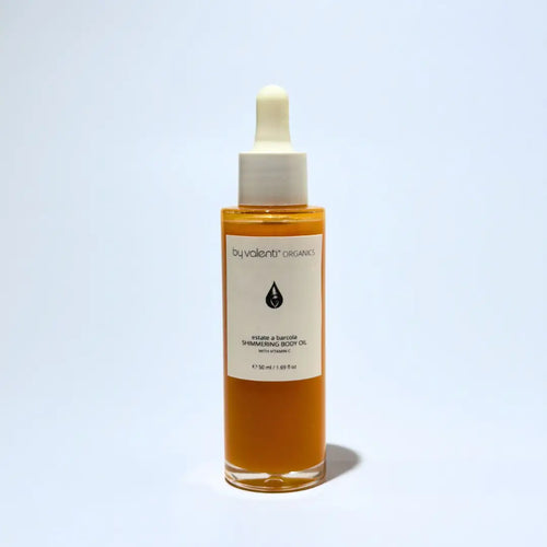 Bottle of By Valenti Organics shimmering body oil with dropper on a light blue background