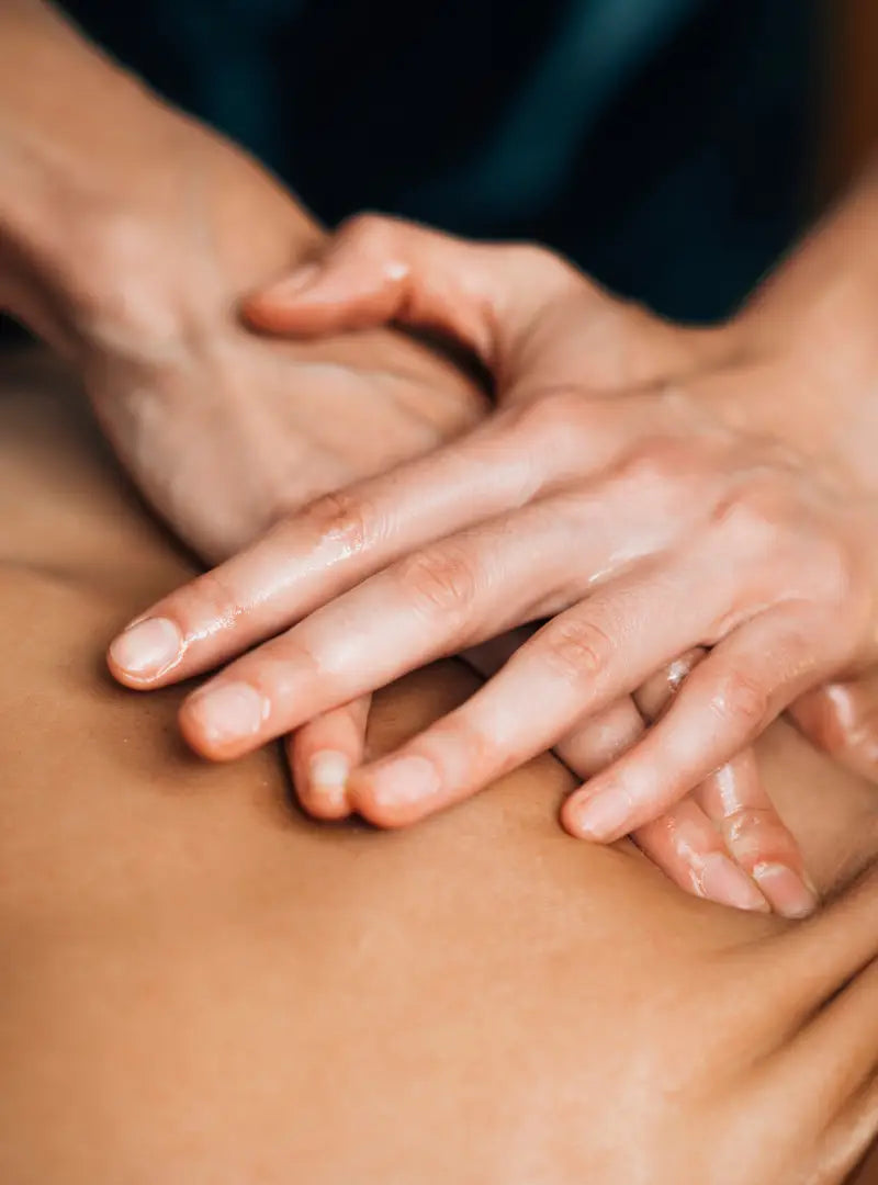 Close-up of hands giving a massage with By Valenti body oil on a person's back