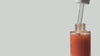 Shimmering body oil from By Valenti dripping into a bottle with a light gray background